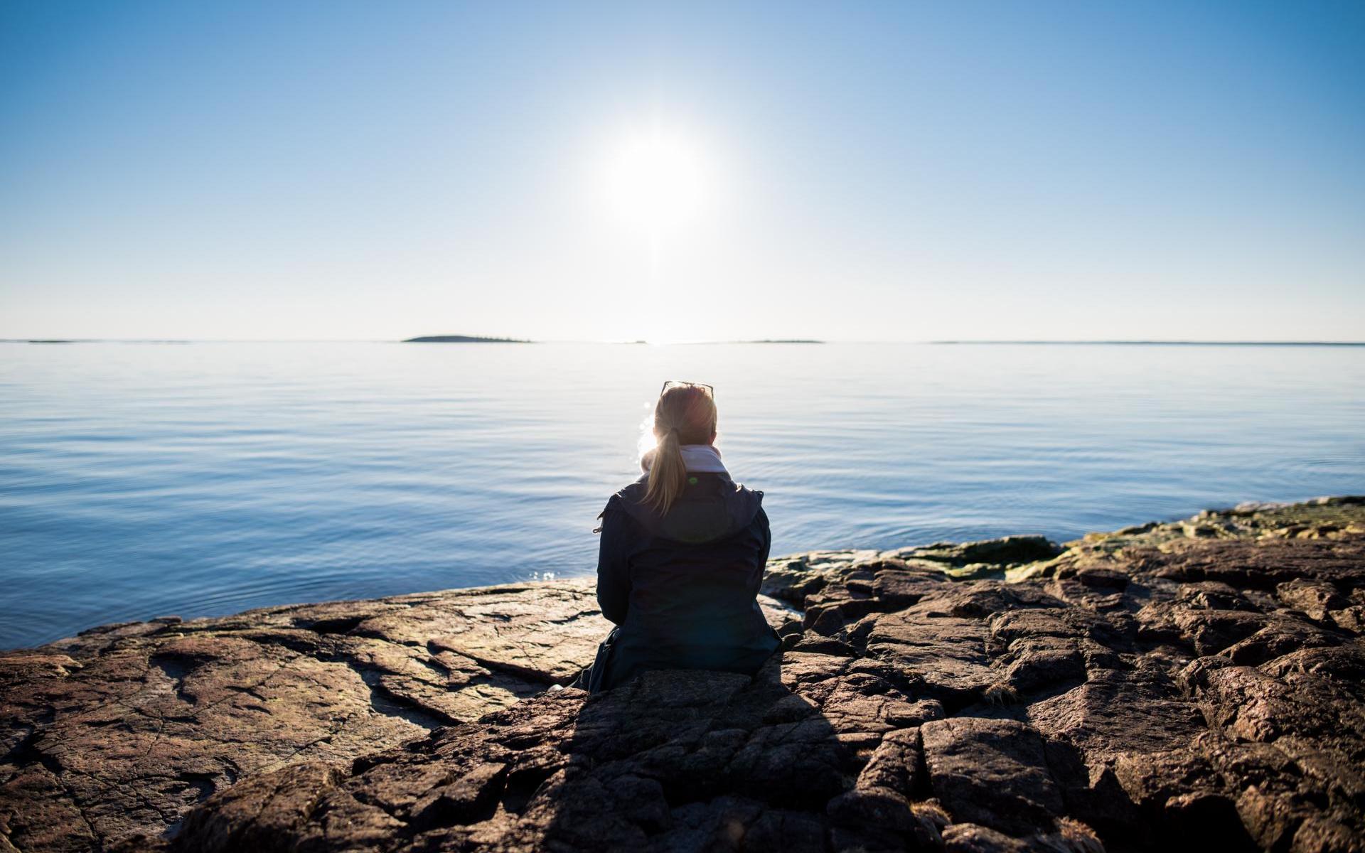 Kvinna njuter av solvarma klippor och ser ut över vattnet